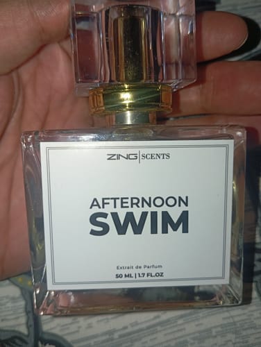 A reviewer holding the clear glass bottle of Afternoon Swim perfume.