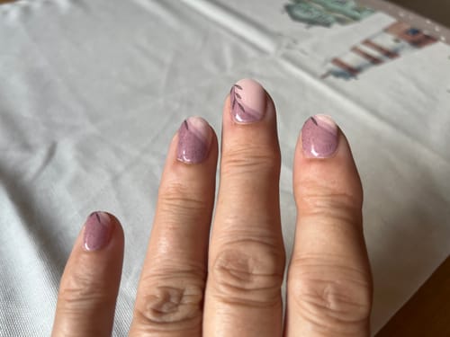 Hand einer Kundin, die ihre manikürten Nägel mit den 'Stone Minimalist' UV-Gel-Nagelfolien in einem abstrakten Design zeigt.