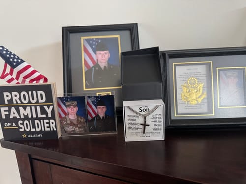 Reviewer's 'To My Son' artisan cross gift set displayed on a table among framed photos of a soldier and an American flag.
