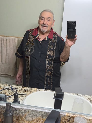 Customer taking a mirror selfie wearing the black El Jefe Azteca Guayabera shirt with a red collar and gold print.