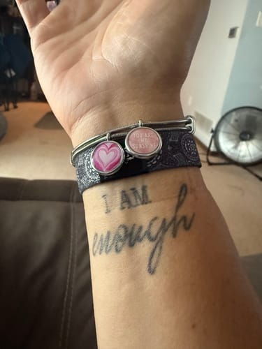 Reviewer's wrist showing a Heart Charm Bracelet with two pink charms combined on one band, layered over another bracelet.