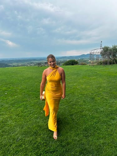 Reviewer smiling in a yellow Celeste Elegant Satin Halter Dress while standing in a grassy field.