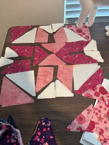 Customer's pre-cut pink and white fabric pieces from the Mystic Scrappy Stars quilt kit laid out on a dark wood table.