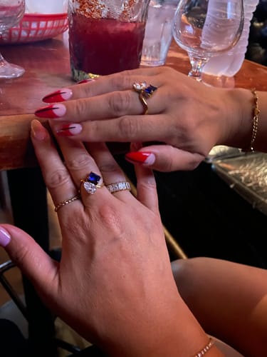 Two reviewers showing their matching Navae Birthstone Rings, each with a blue and a clear stone.