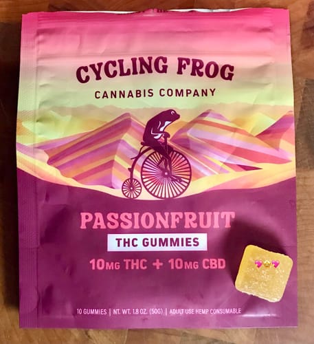 Reviewer's colorful pouch of Passionfruit Gummies with a single square gummy sitting beside it on a wooden surface.