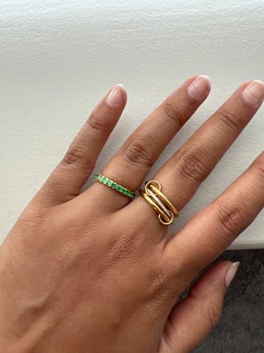 Customer wearing the gold Eterna Birthstone Ring with green stones, stacked with another ring on their finger.