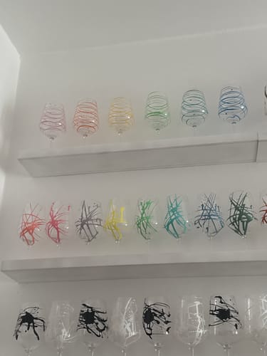 Il cliente mostra i suoi calici in vetro colorati con motivi a spirale e a schizzi, esposti su tre mensole.