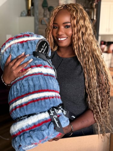 Reviewer smiling while holding the plush, folded Hugs Patriotic Stripe Blanket.