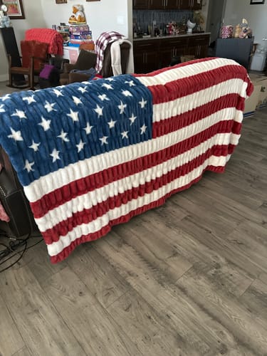 Reviewer's plush Hugs Flag Blanket draped over the back of a living room couch.