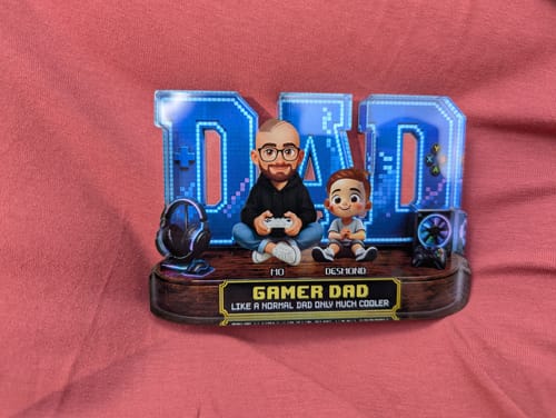 Customer's personalized 'Gamer Dad' figurine featuring a father and child, set against a pink background.