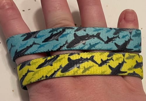 Customer's hand holding two Dundun Mystery Bracelets. One is blue and one is yellow, both with a shark design.