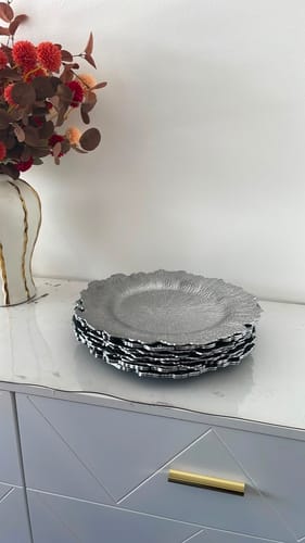 Customer's stack of decorative silver plates with textured edges sitting on a white cabinet.