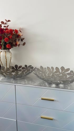 Customer's two decorative silver bowls with a cutout leaf pattern on a white cabinet.