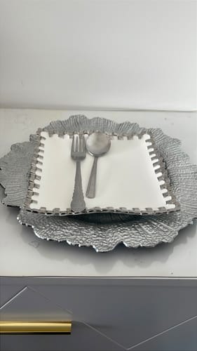 Reviewer's place setting with a square white plate and silverware on a decorative silver charger.