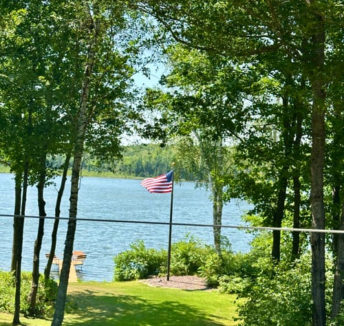 Customer's Ultra Heavy Duty American Flag waving on a flagpole in a yard by a lake.