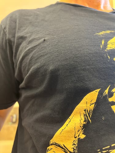 Close-up of a customer wearing the dark Lincoln 250 T-Shirt, showing a small hole in the fabric on the chest.