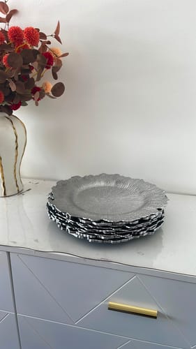 Customer's stack of decorative silver plates with textured edges sitting on a white cabinet.