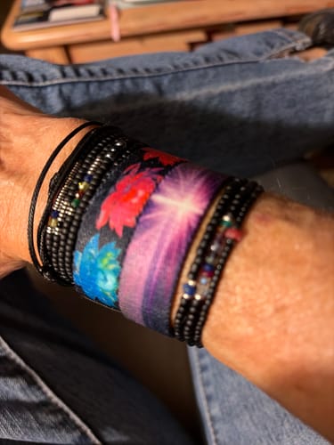 Customer's wrist wearing the colorful Despite My Trials Bracelet with a lotus design, stacked with other bracelets.