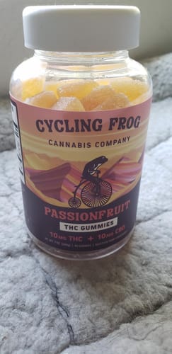 Customer's bottle of Cycling Frog Passionfruit Gummies on a textured gray surface, with the yellow gummies visible inside.