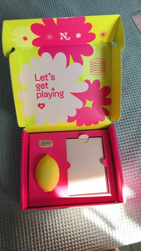 Customer's yellow Lem Clitoral Massager inside its open and vibrant pink and yellow box.
