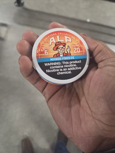 Reviewer's hand holding a white tin of ALP Drifters Mango Freeze nicotine pouches.