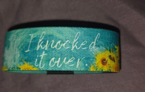 Customer's teal 'I Knocked It Over' bracelet with white text and a sunflower design.
