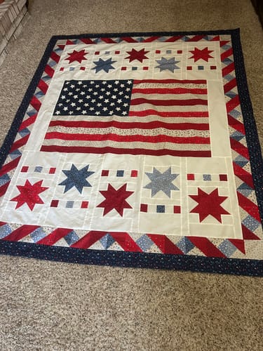 Customer's finished Freedom Song Quilt spread out on a carpeted floor, showing the full patriotic flag and star design.