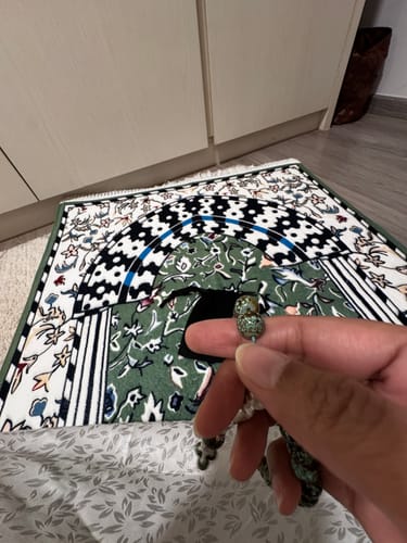 Customer's hand holding prayer beads over the patterned Minbar Al Rawda Padded Prayer Mat.