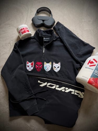 Customer's black Demon Slayer quarter-zip with embroidered masks on the chest, laid flat with other items on a gray surface.