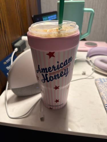 Customer's pink and white American Honey To-Go Buddy insulator holding a cup with an iced drink on a desk.