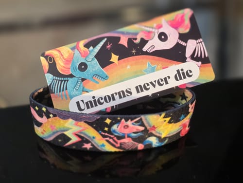 Close-up of a 'Unicorns never die' wristband from a customer's Mystery 3-Pack, showing colorful skeleton unicorn artwork.