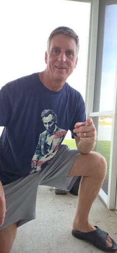 Reviewer smiling while wearing the dark blue Lincoln America T-Shirt with its Abe Lincoln guitarist graphic.