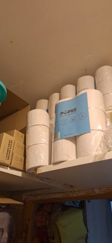 Client montrant des rouleaux de papier toilette double épaisseur stockés sur une étagère haute.