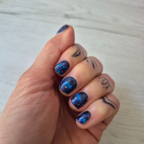 Kunde zeigt die aufgetragenen UV-Gel-Nagelfolien 'Midnight Thoughts' mit blauem Blumenmuster.