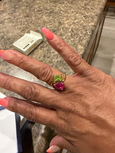 Customer's hand wearing the Navae Birthstone Ring with a vibrant green rectangular stone and pink pear-shaped stone.