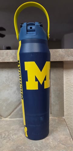 Customer's navy Bottle Buddy featuring the yellow Michigan Wolverines logo, standing on a counter.