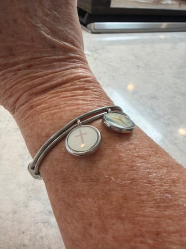 Customer wearing the Cross Charm Bracelet with two round charms, one white with a cross, on their wrist.