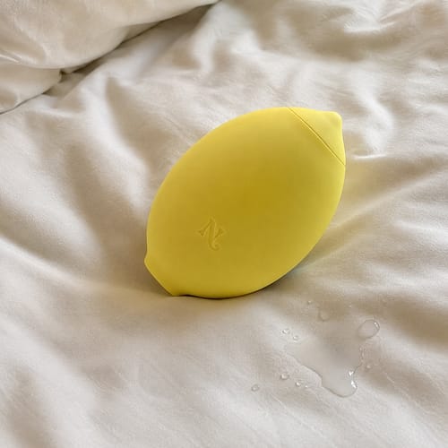 Customer's yellow Lem Clitoral Massager resting on rumpled white sheets with a splash of clear liquid.