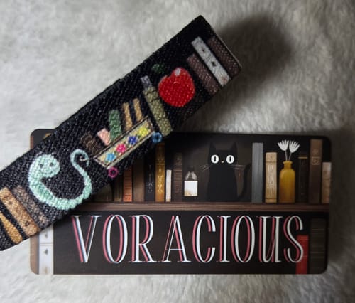 Customer's Voracious Bracelet showing the book-themed design, placed on top of its matching collector card.