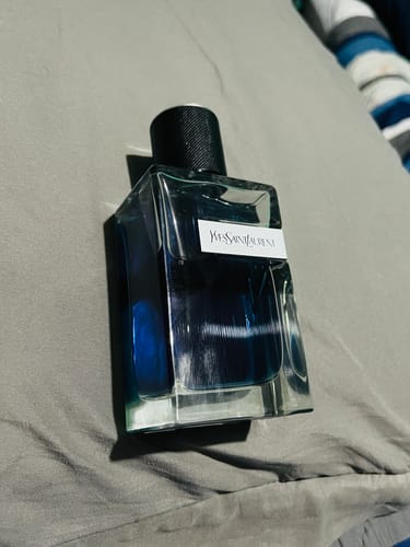 Cliente muestra el frasco del perfume YSL Y Iced Cologne acostado sobre una superficie gris.