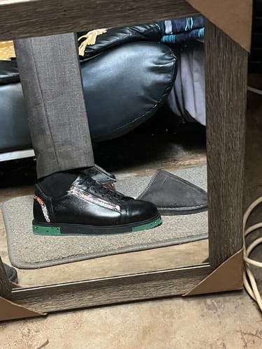 A reviewer's foot in a black LUFIANO leather sneaker with a bright green sole and a patterned side detail.