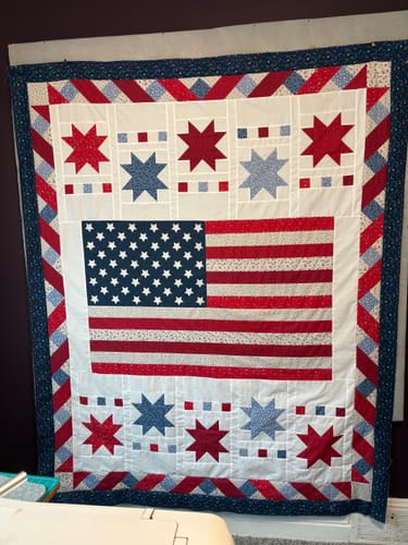 Customer's completed Freedom Song quilt hanging on a wall, showing the patriotic flag and star pattern.