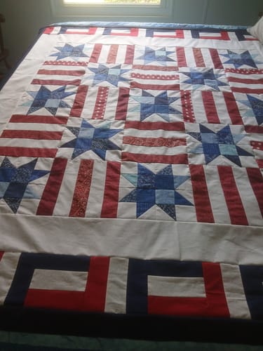 Customer's completed Red, White, and Cute quilt draped on a bed, showing the patriotic star and stripe pattern.
