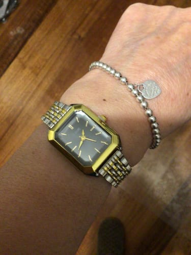 Customer's CLAIRE DE MAINS watch with a gold case and two-tone band worn on their wrist.