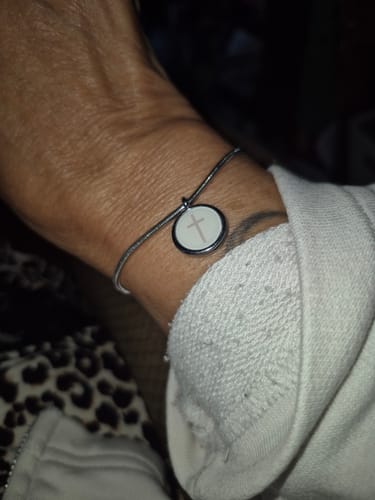 Customer wearing the Cross Charm Bracelet on their wrist, showing the round white charm with a cross.