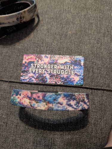 Customer's Stronger With Every Struggle Bracelet shown with its matching collector's card on a dark fabric surface.