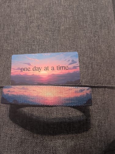 Reviewer's One Day At A Time Bracelet and matching card, both featuring a colorful sunset design, laid on a gray surface.