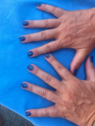 Die Hände einer Kundin mit aufgetragenen 'Midnight Thoughts' UV-Gel-Nagelfolien mit blauem Blumenmuster.