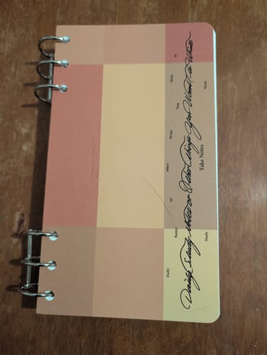 Customer's Index 3.0 Color Block notebook with a colorful cover and six-ring binding, lying on a wooden surface.