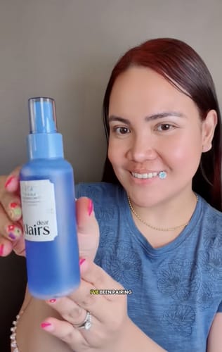 Reviewer smiling while holding the blue bottle of Blue EGF Calming Mist.